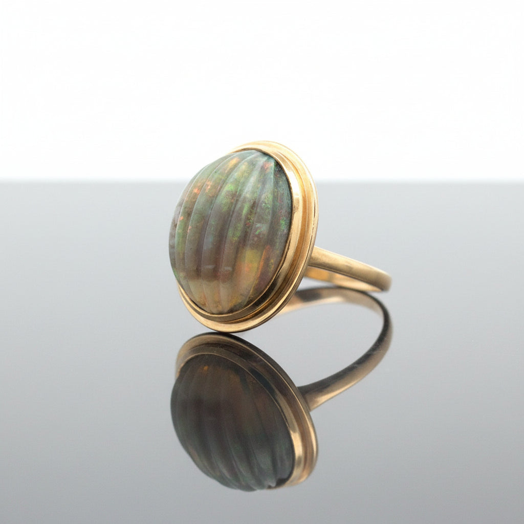 A vintage ring featuring a large, oval carved opal cabochon set in a gold bezel, with a gold band, shown on a plain white background.