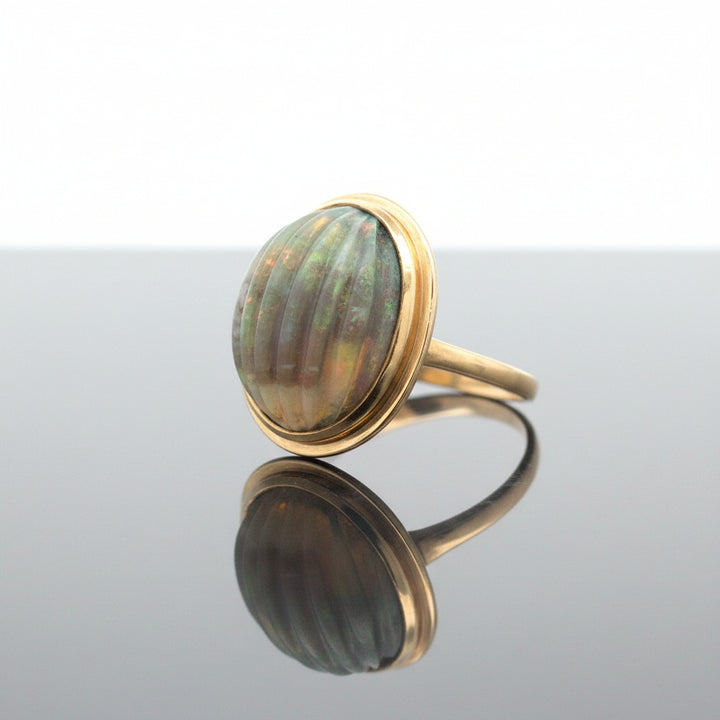 A vintage ring featuring a large, oval carved opal cabochon set in a gold bezel, with a gold band, shown on a plain white background.