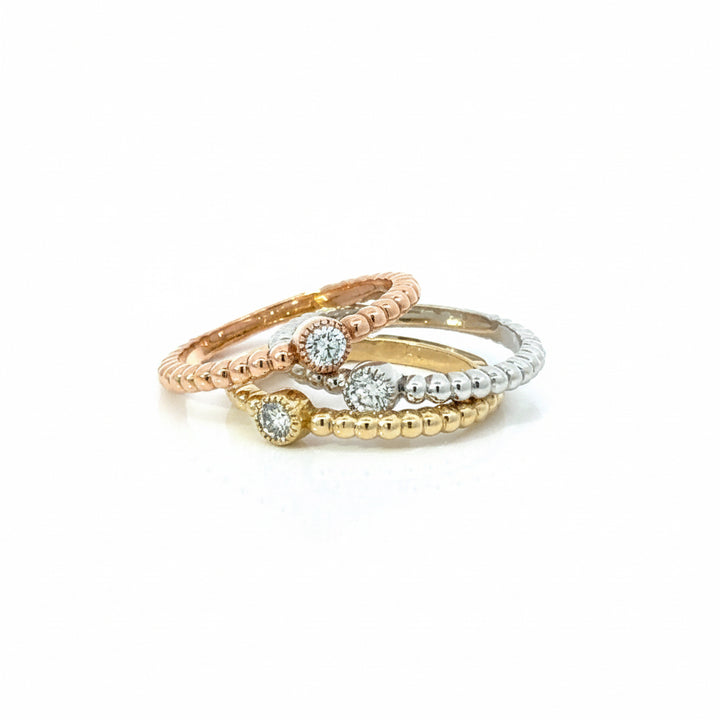 Three stacked rings on a white background: a rose gold beaded band with a round-cut diamond, a yellow gold beaded band with a round-cut diamond, and a silver beaded band with a round-cut diamond.